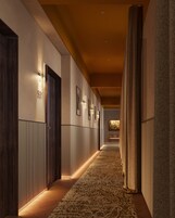 Un corridoio con tappeto decorato, porte in legno e lampade a parete.