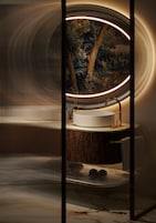 A modern bathroom with a round sink, a mirror, and a decorative tree mural on the wall.