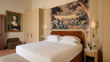 Ein Hotelzimmer mit einem großen Bett, einem mit einem Gemälde verzierten Kopfteil, einem Nachttisch mit Lampe und einer Sitzbank.