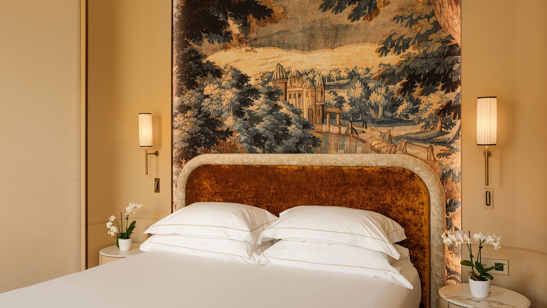 Ein Hotelzimmer mit einem großen Bett, zwei Nachttischen mit Lampen und einem Wandteppich mit Landschaftsmotiv.