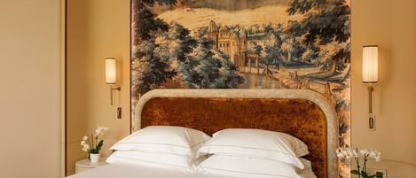 A hotel room with a large bed, two bedside tables with lamps, and a tapestry depicting a landscape.