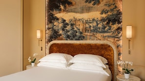 Una habitación de hotel con una cama grande, dos mesitas de noche con lámparas y un tapiz que representa un paisaje.