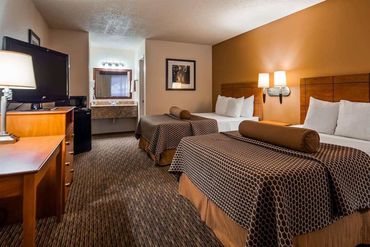 A hotel room with two beds, a desk, a television, a bathroom, and a painting on the wall.