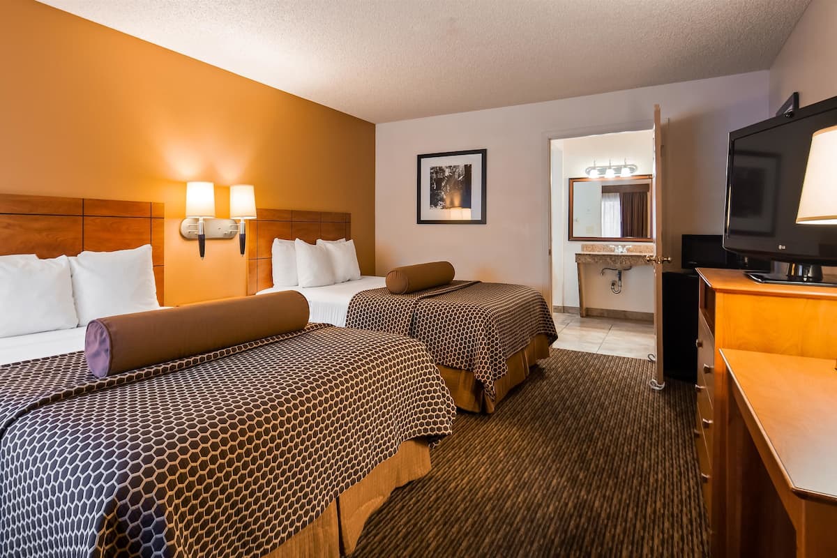 A hotel room with two beds, a TV, a desk, and a bathroom visible through an open door.