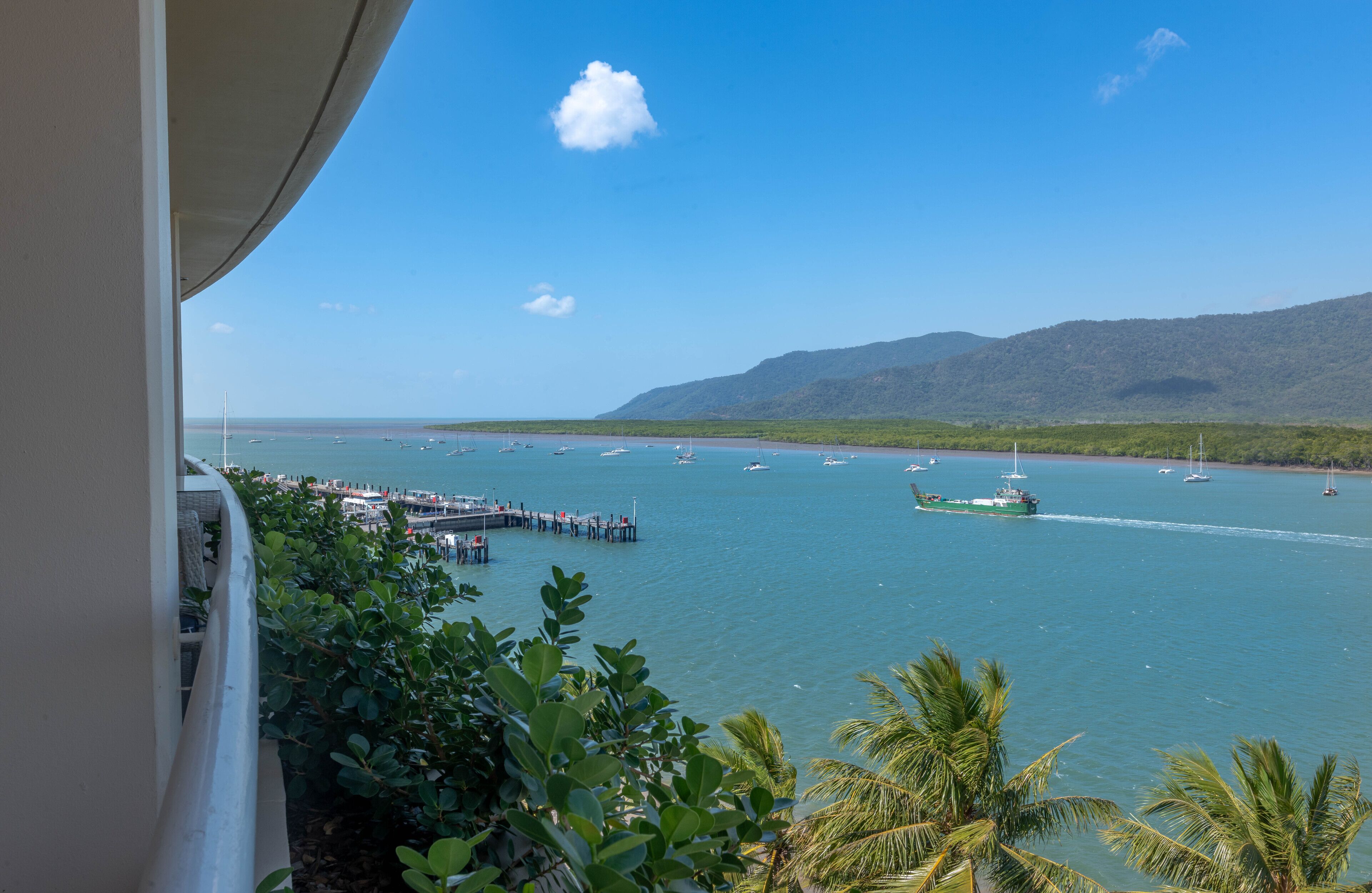 A coastal view with a pier extending into the water, boats, and a mountainous backdrop.