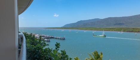 A coastal view with a pier extending into the water, boats, and a mountainous backdrop.