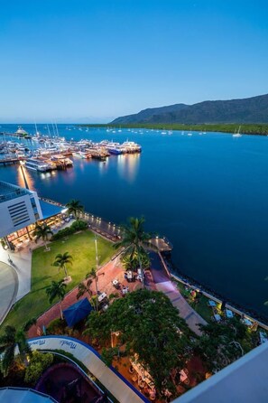 A marina with boats docked, a restaurant with outdoor seating, and a view of the water and hills in the background. - Hilton Cairns (Cairns)