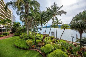 A landscaped garden with palm trees, a water body, and a view of a mountain range.