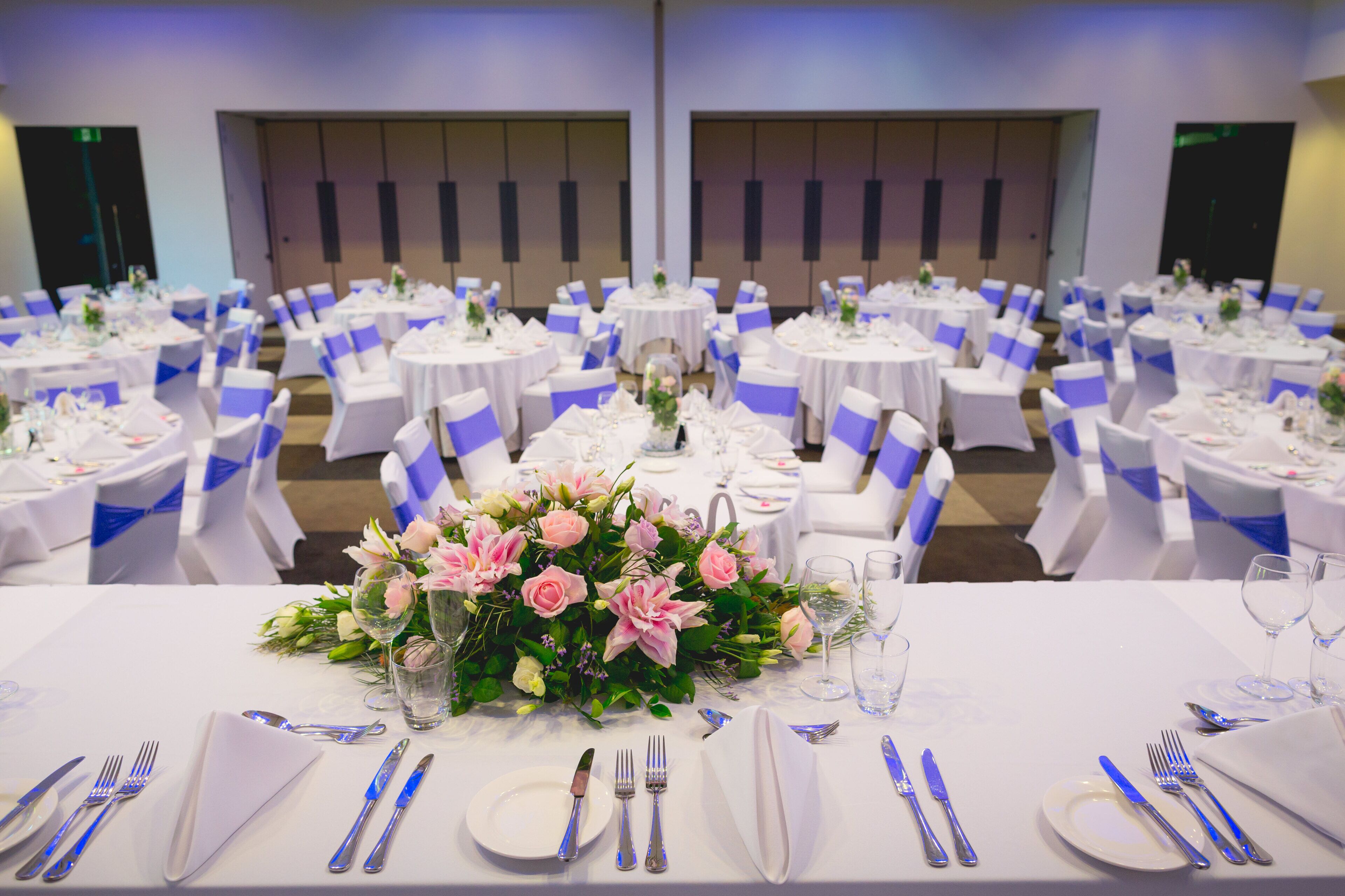 A banquet hall with round tables, white tablecloths, and blue sashes.