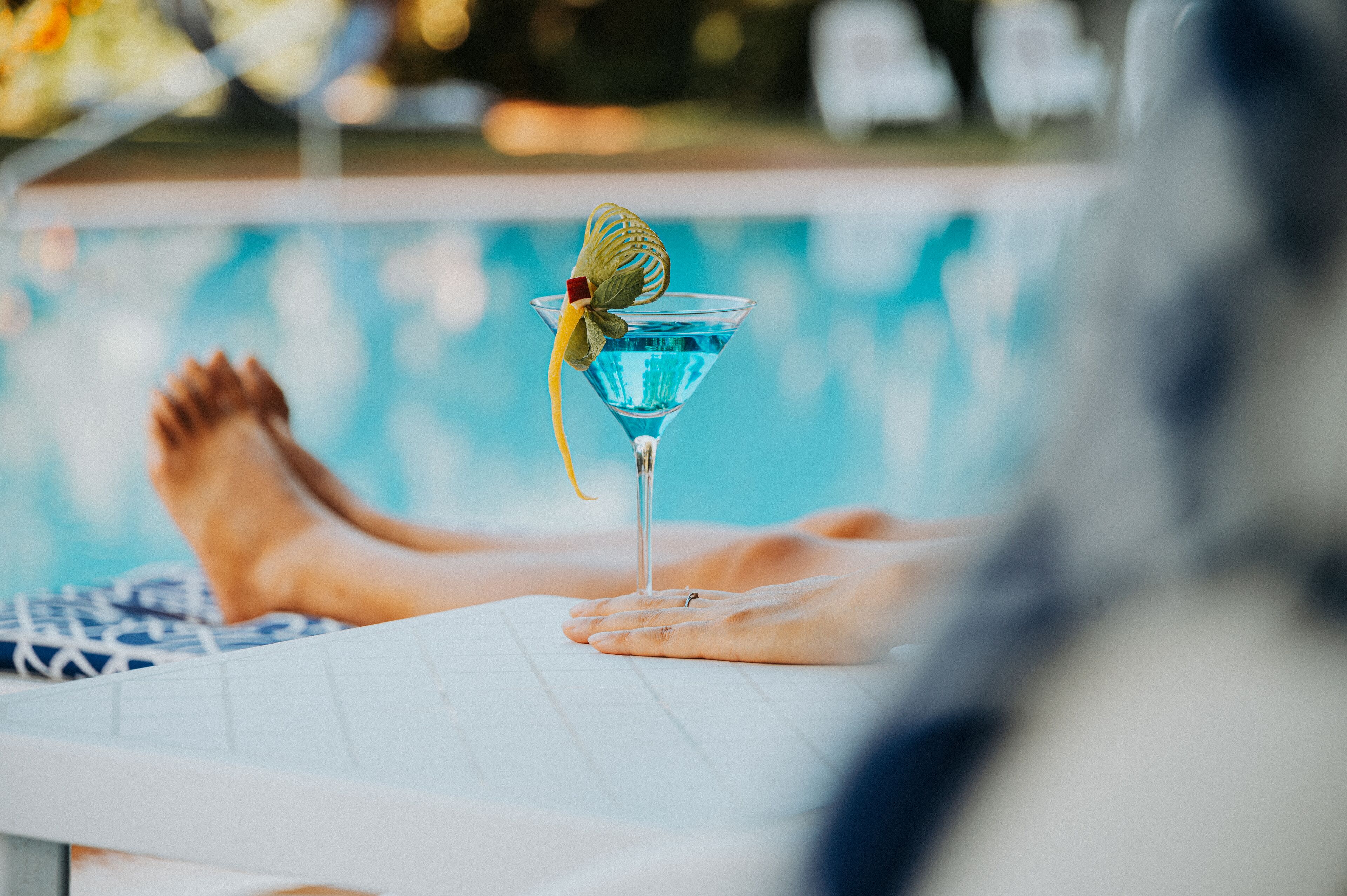Escena junto a una piscina con una copa de martini sobre una mesa blanca.