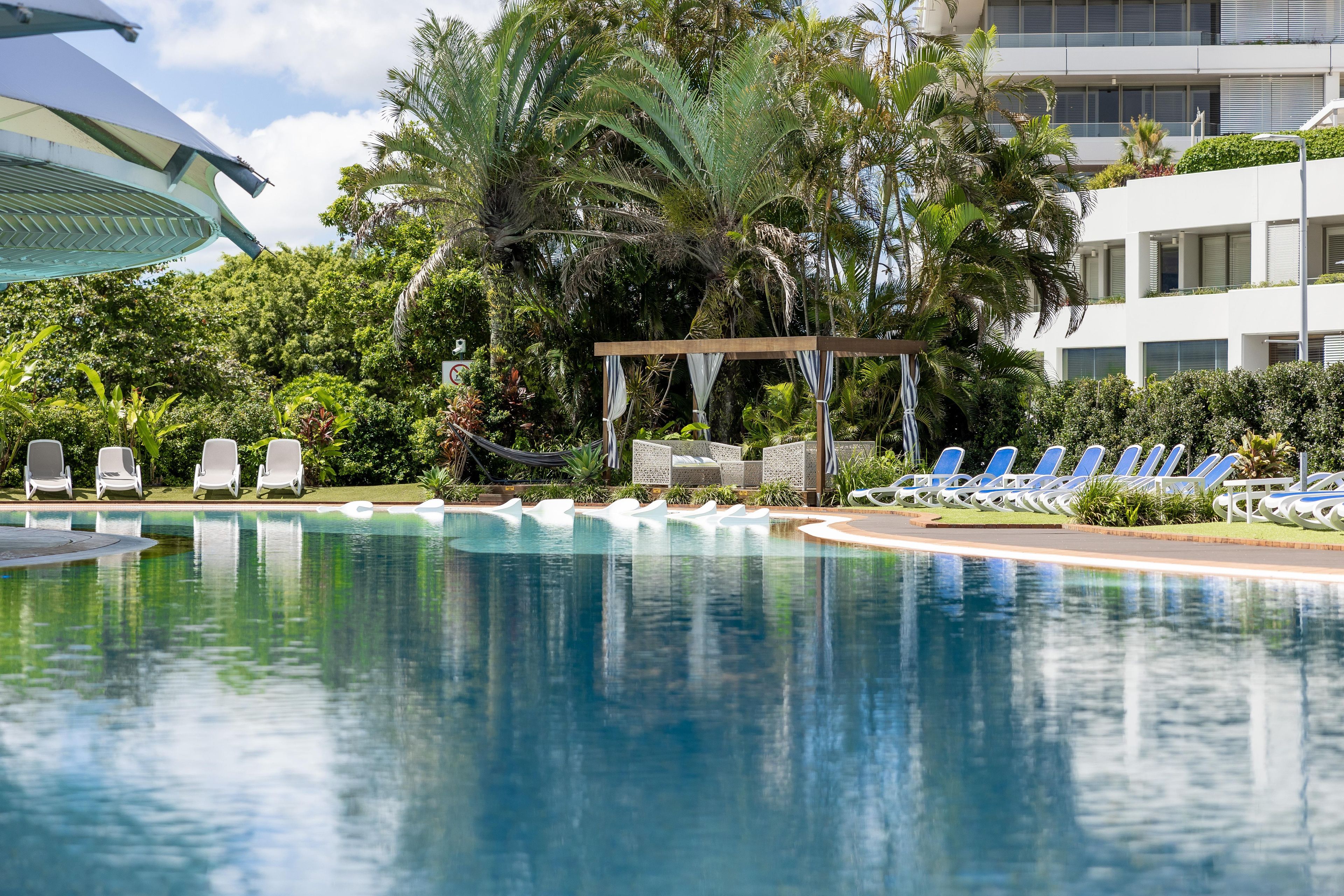 A swimming pool with lounge chairs and a pergola surrounded by lush greenery.