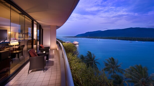 A balcony with a view of the sea, a dining area with chairs and a table, and a glass wall reflecting the interior. - Hilton Cairns (Cairns)