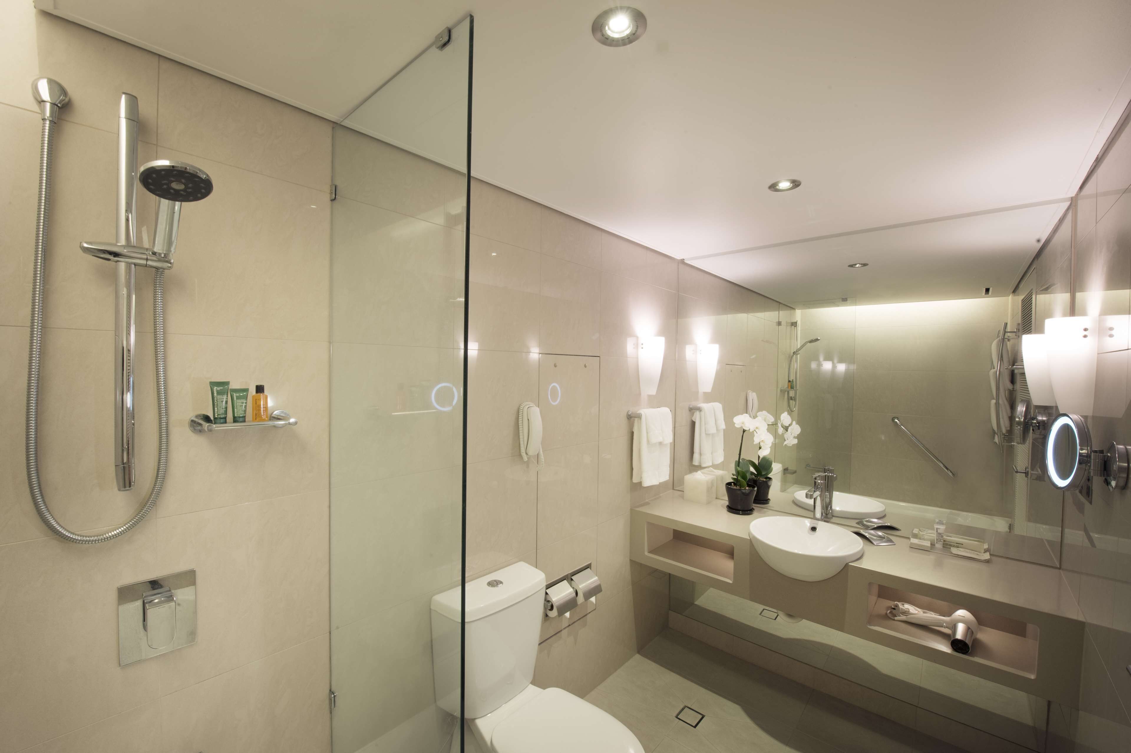 A modern bathroom with a glass-enclosed shower, a toilet, a sink with a mirror, and a vanity with toiletries.