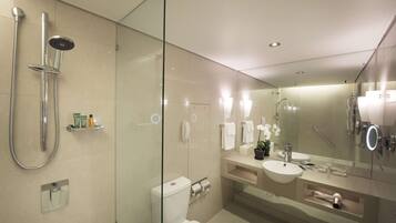 A modern bathroom with a glass-enclosed shower, a toilet, a sink with a mirror, and a vanity with toiletries.