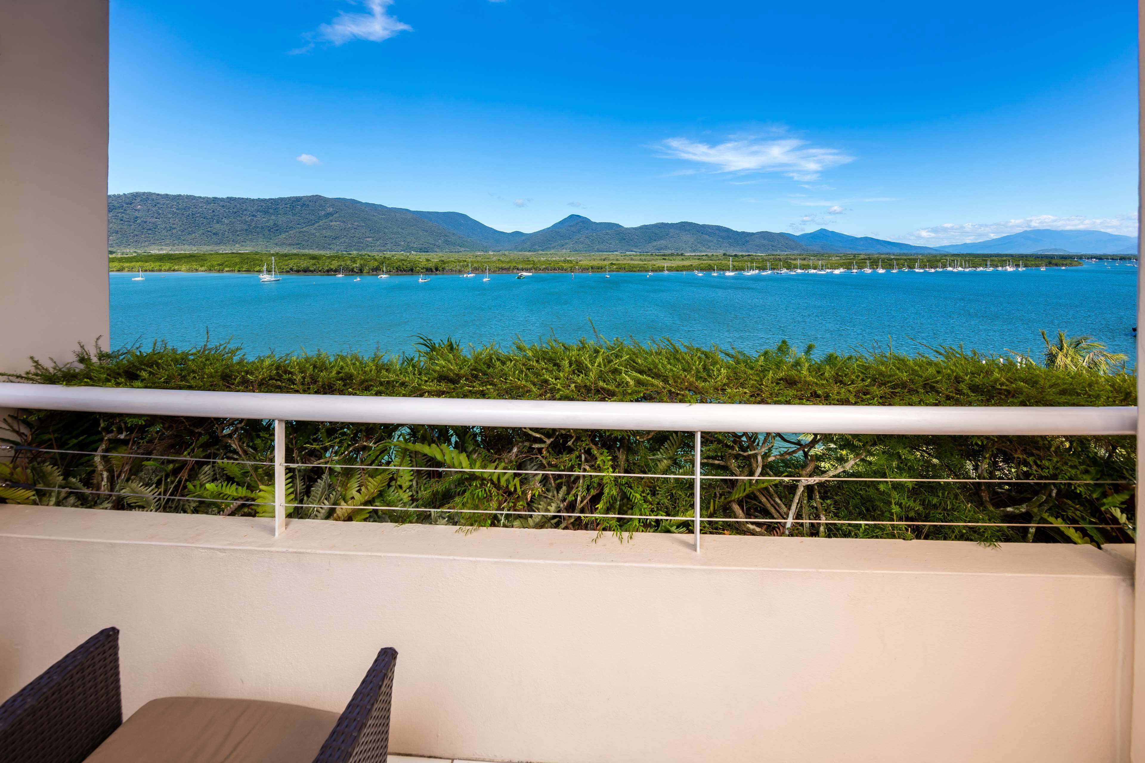 A balcony with a view of a calm lake, surrounded by greenery and mountains in the distance.