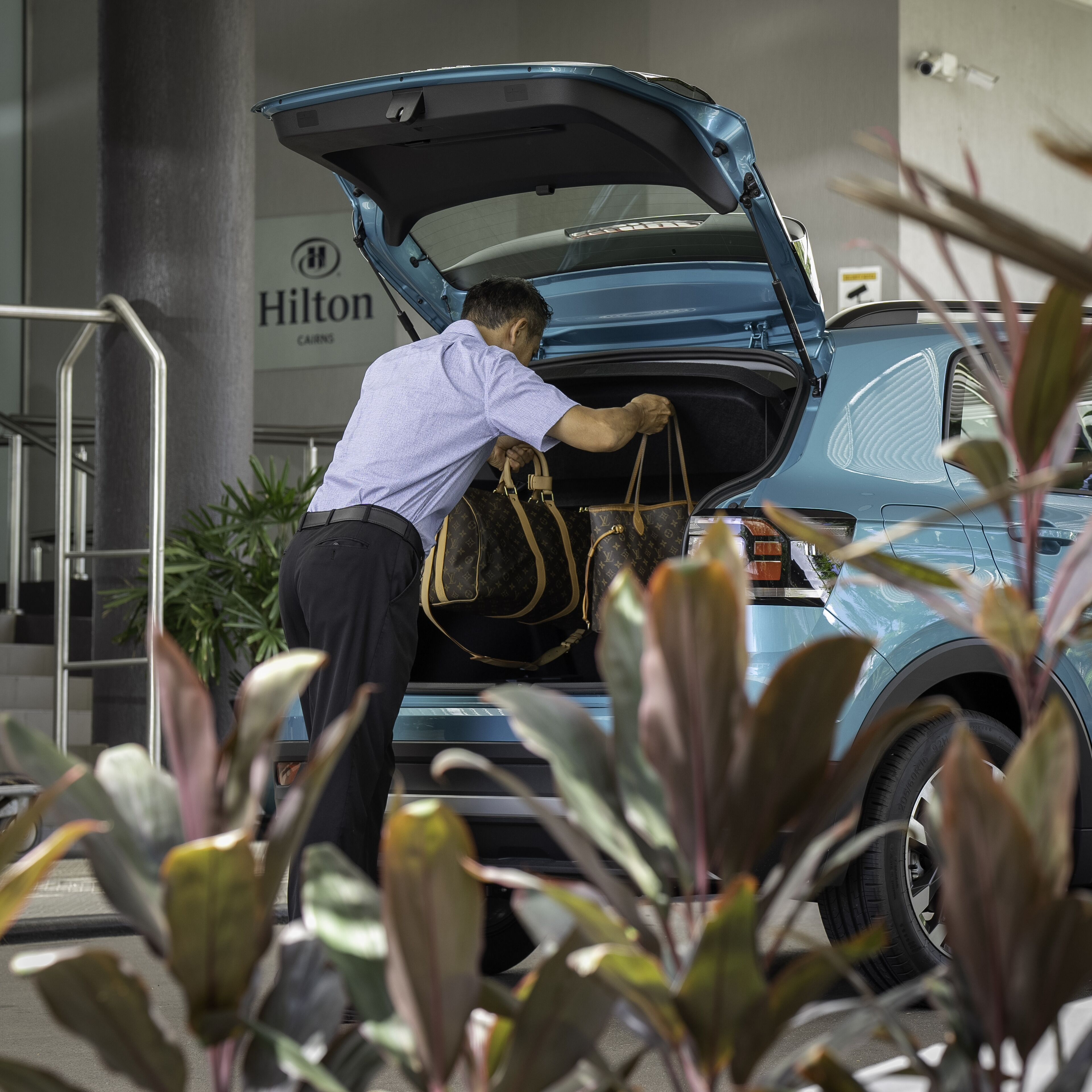 Een man plaatst een Louis Vuitton tas in de kofferbak van een auto bij een hotel.