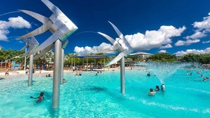 A large outdoor swimming pool with clear blue water, surrounded by palm trees and a pavilion. - Hilton Cairns (Cairns)