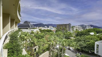 A view from a balcony overlooking a cityscape with buildings, palm trees, and mountains in the background.
