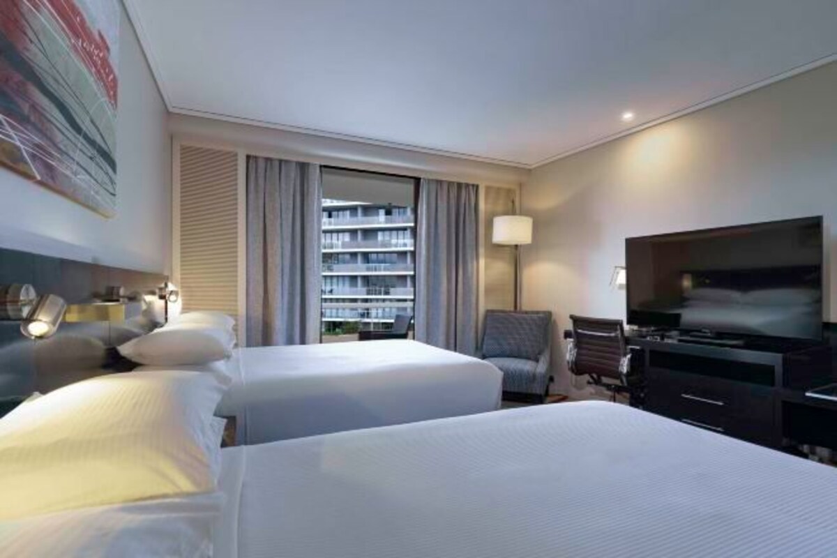 Habitación de hotel con dos camas, televisión, escritorio y ventana con cortinas.