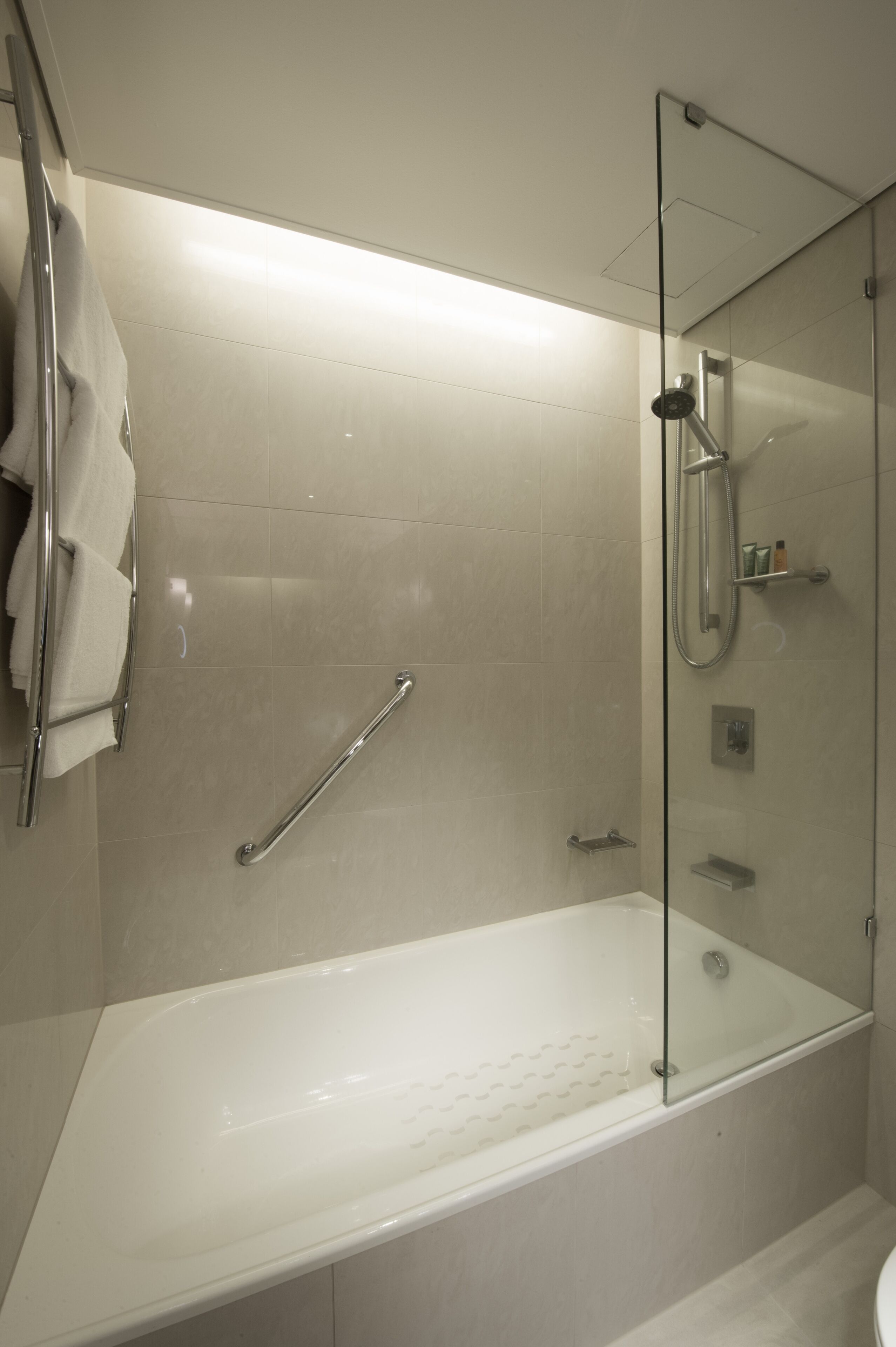 A modern bathroom with a glass-enclosed shower, a white bathtub, and a handrail.