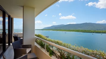 A balcony with wicker furniture overlooking a calm body of water with boats and mountains in the distance.