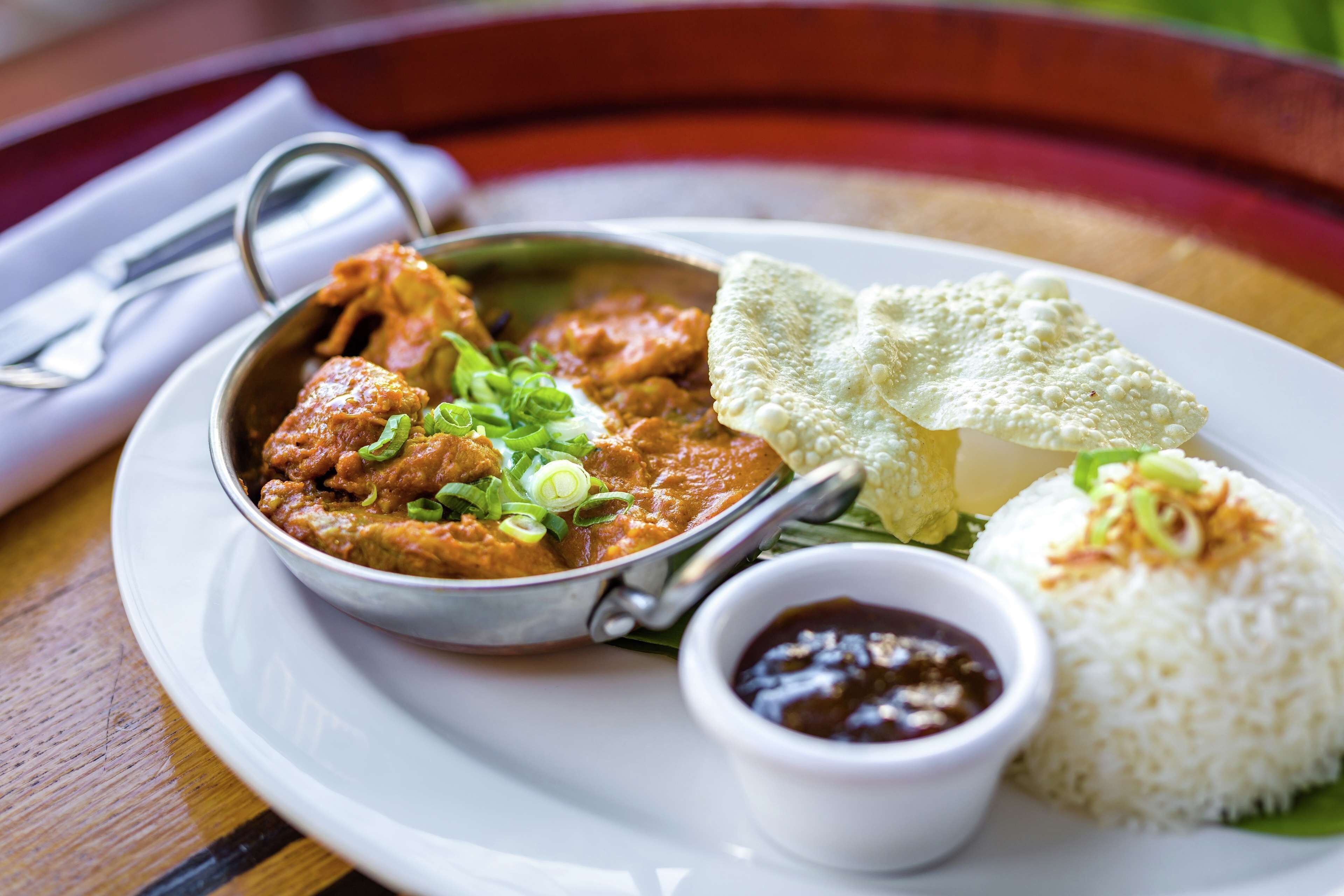 A plate with curry, rice, and a small bowl of sauce.