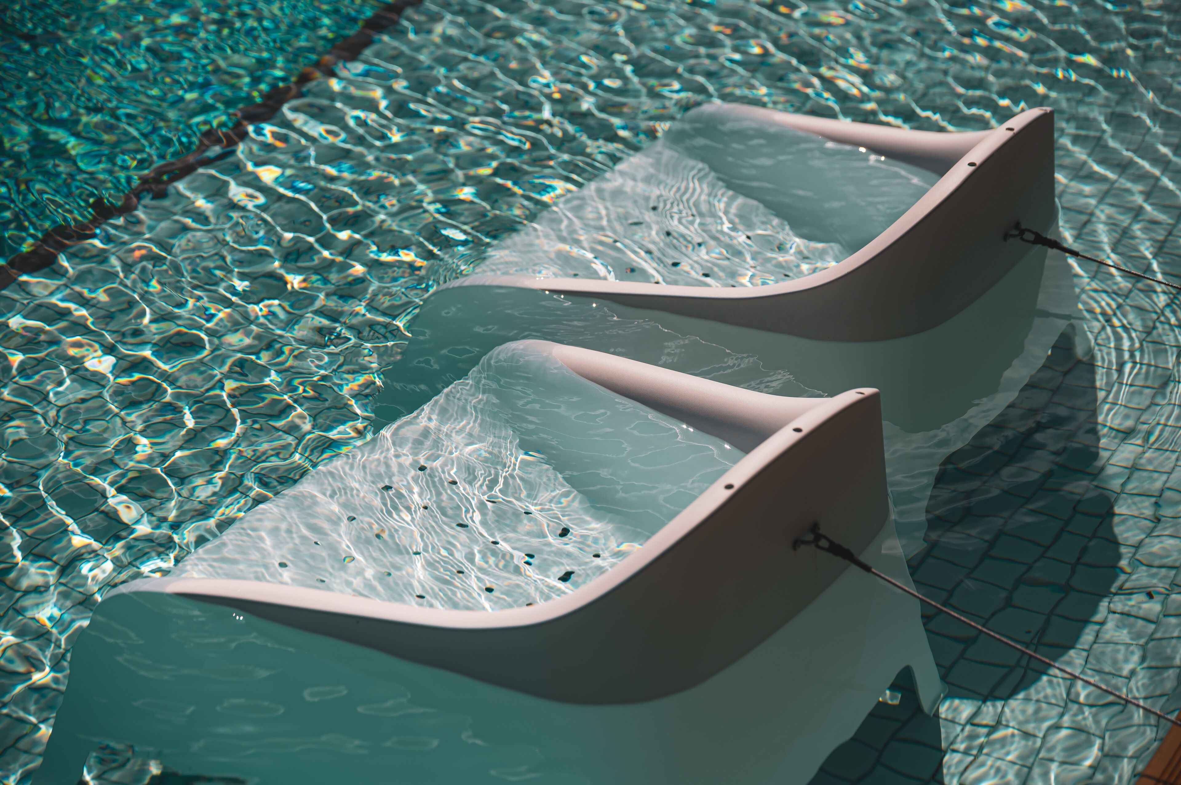 Dos tumbonas en una piscina cristalina con suelo de baldosas.