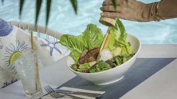 A bowl of salad with a lime wedge and a wooden salt shaker, placed on a table with a striped tablecloth.