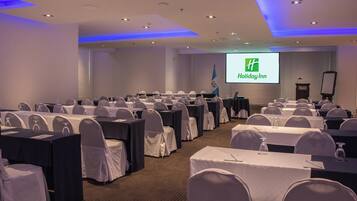 A conference room with rows of tables and chairs, a podium, and a projection screen displaying 'Holiday Inn'.