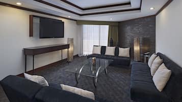 A modern living room with a large flat-screen TV, dark sofas, a glass coffee table, and a patterned carpet.