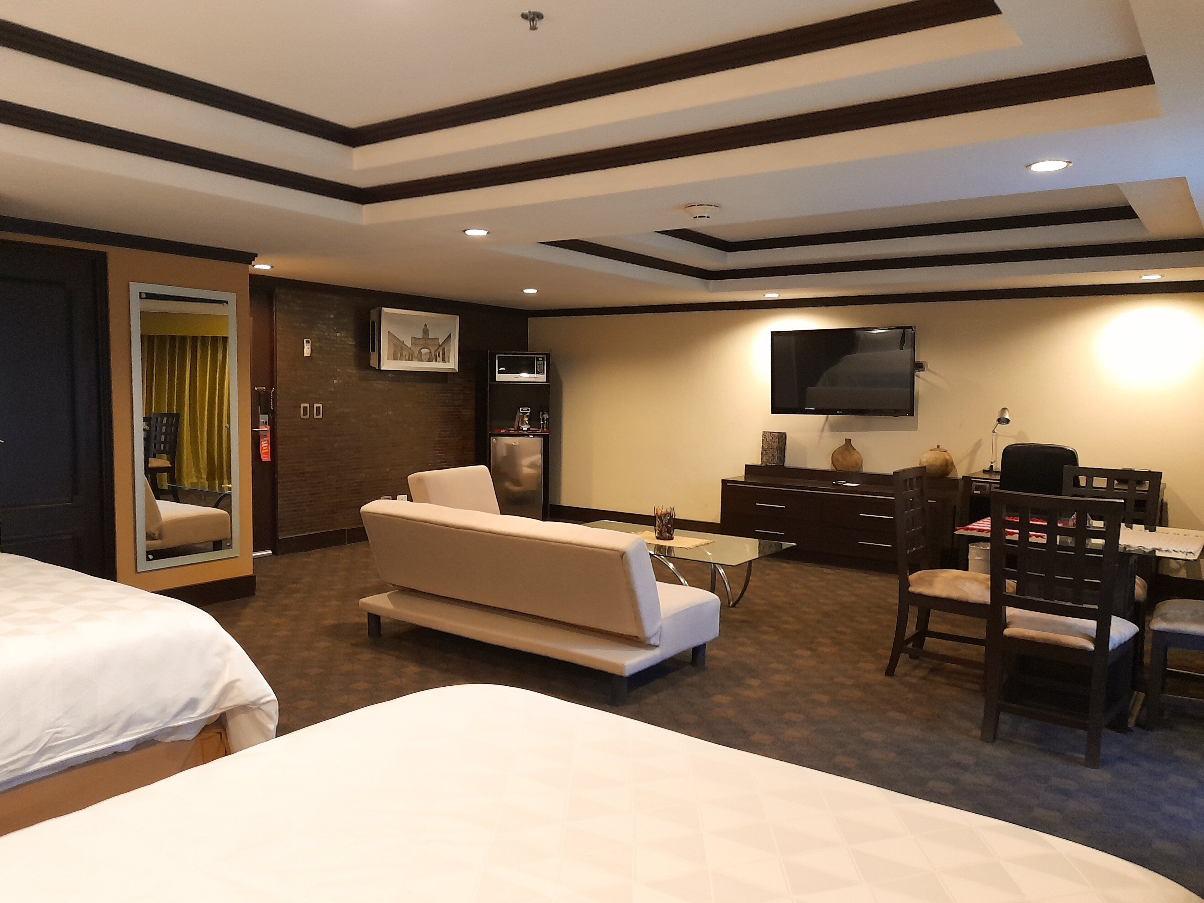 A hotel room with a bed, a sofa, a desk with a chair, a television, and a minibar.