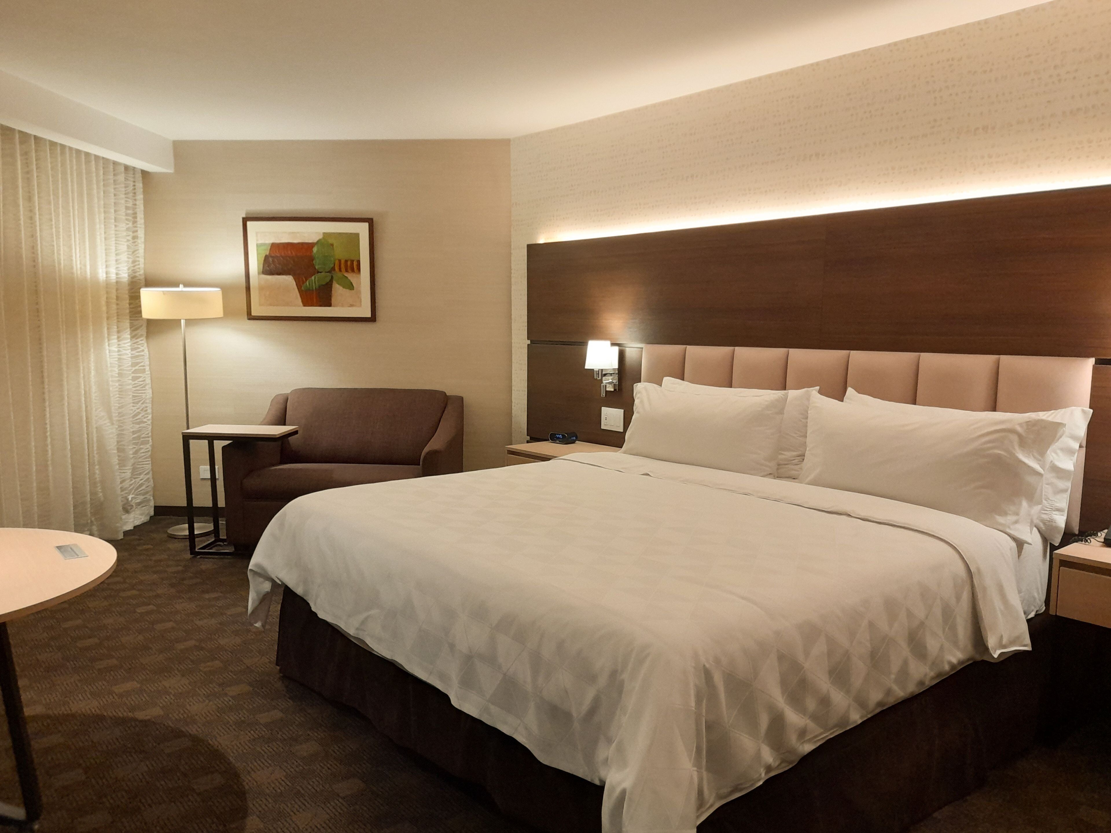 A hotel room with a large bed, a chair, a small table, and a lamp.