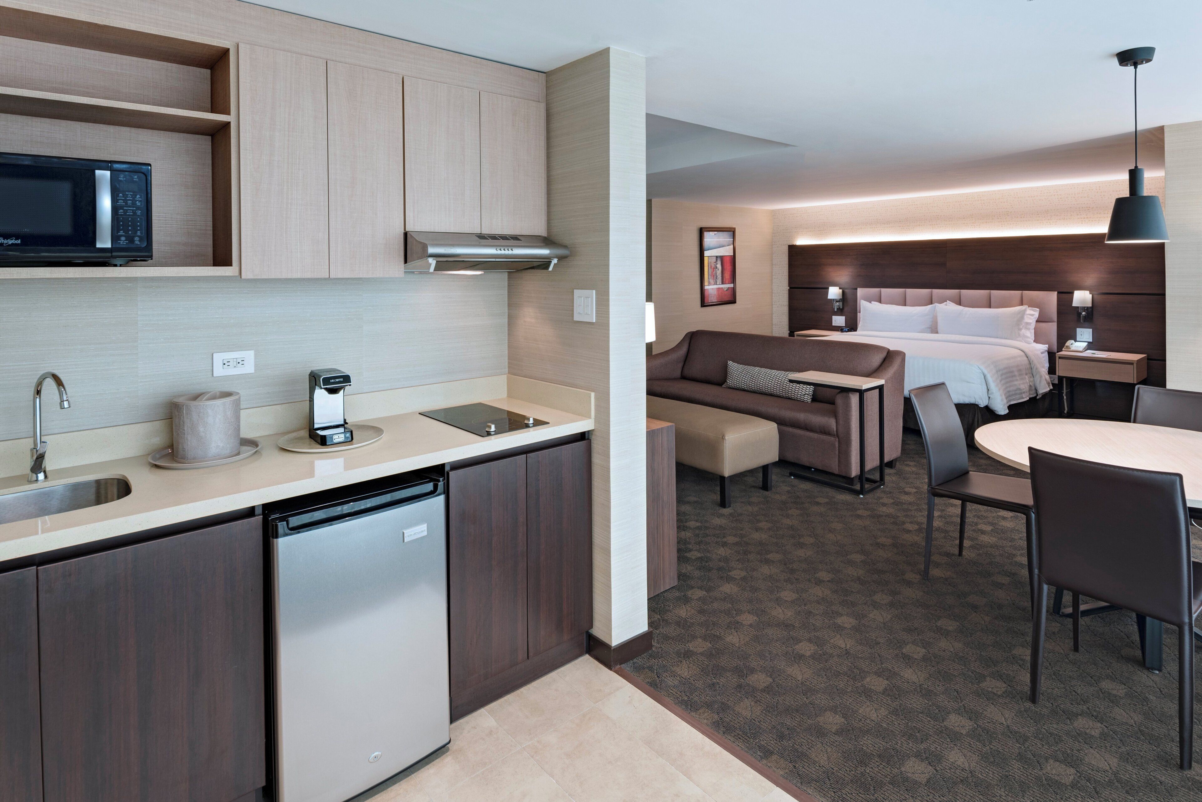 A compact hotel room with a kitchenette, a bed, a sofa, and a dining area.