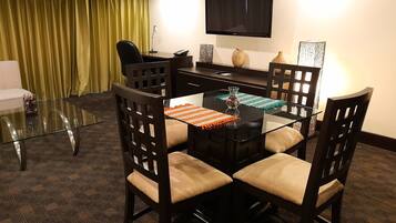 A conference room with a glass table, four wooden chairs, a TV mounted on the wall, and a yellow curtain.