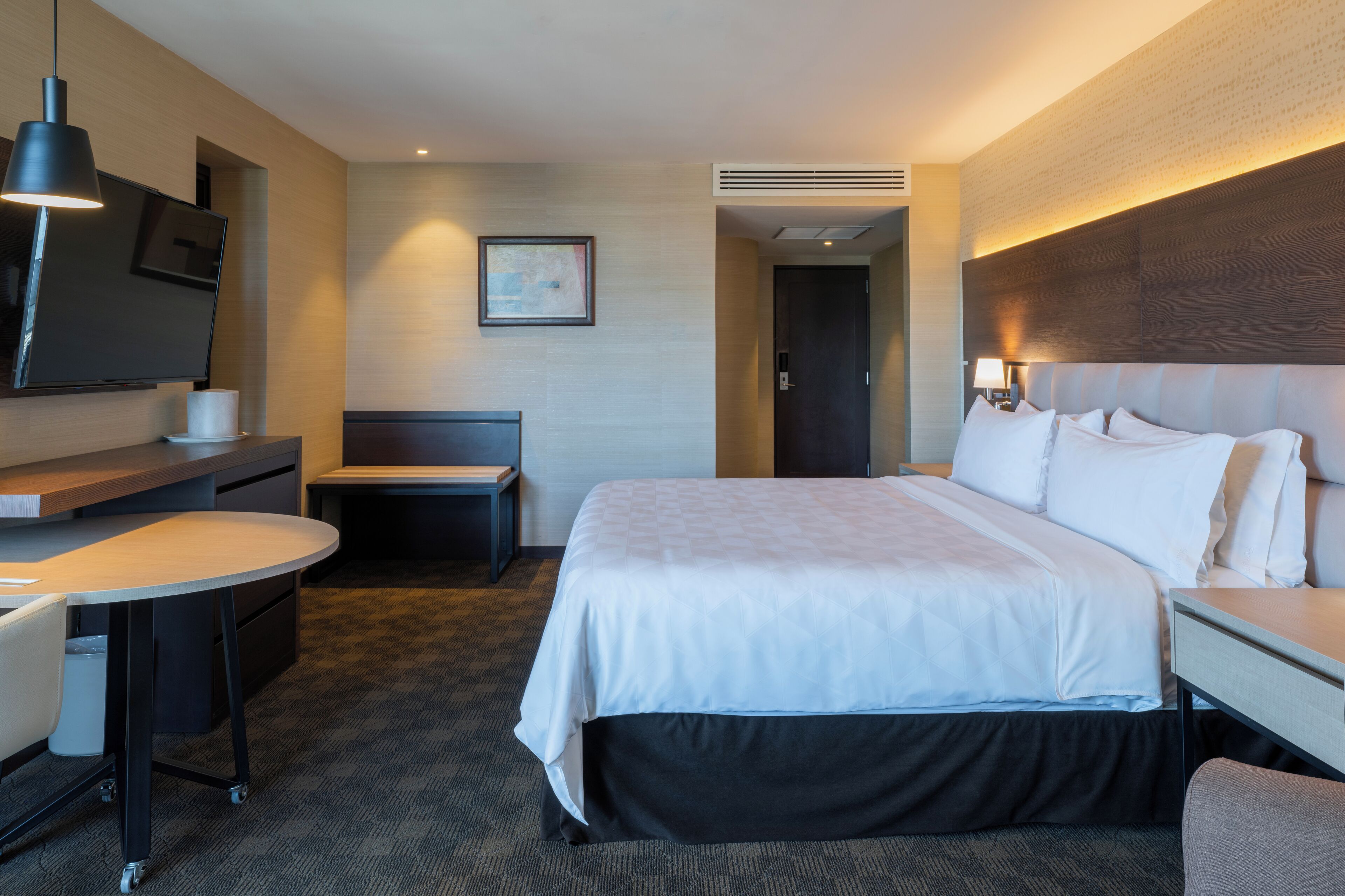 A hotel room with a bed, a desk, a chair, a television, and a framed picture on the wall.