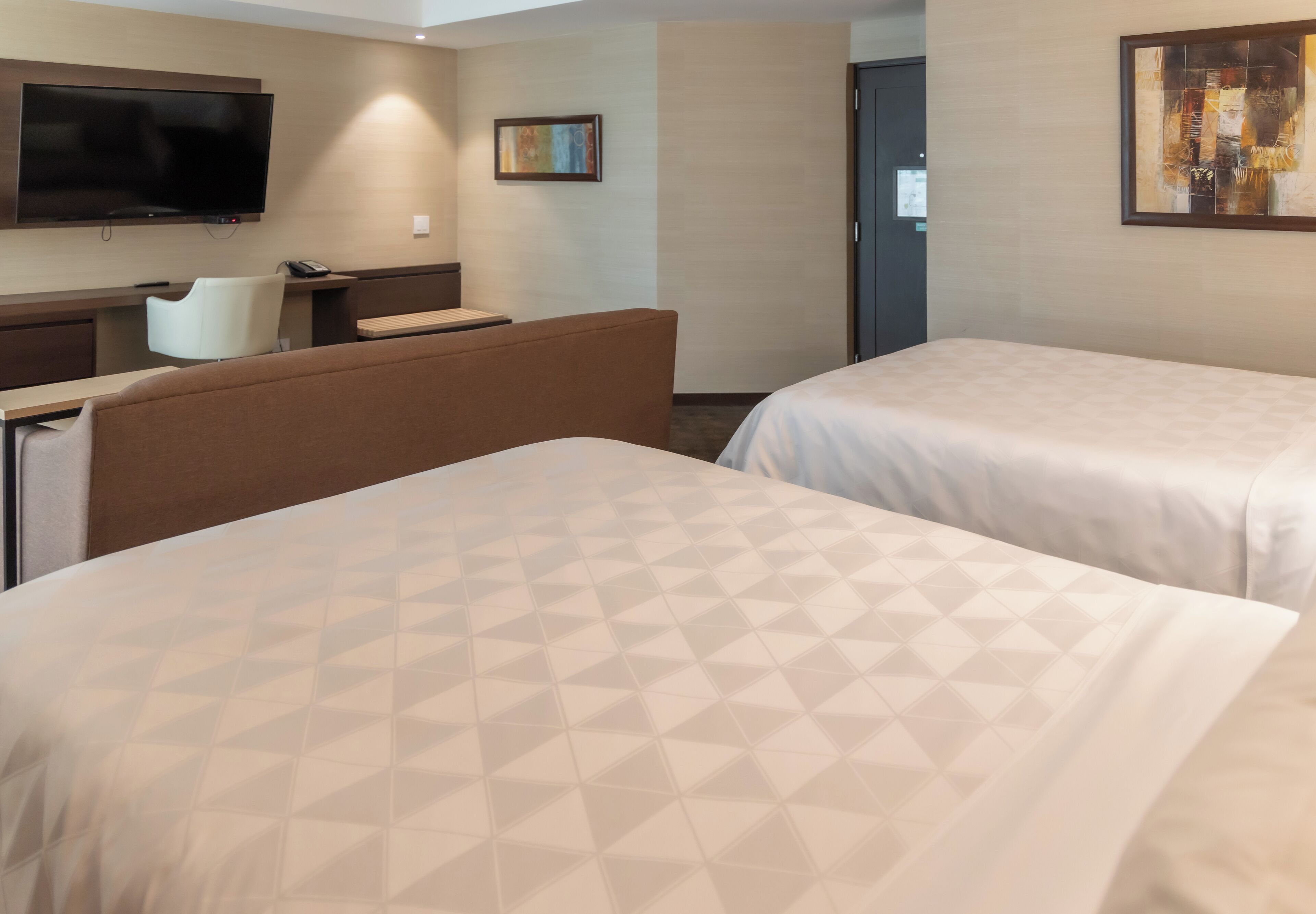 A hotel room with two beds, a desk, a chair, a television, and artwork on the walls.