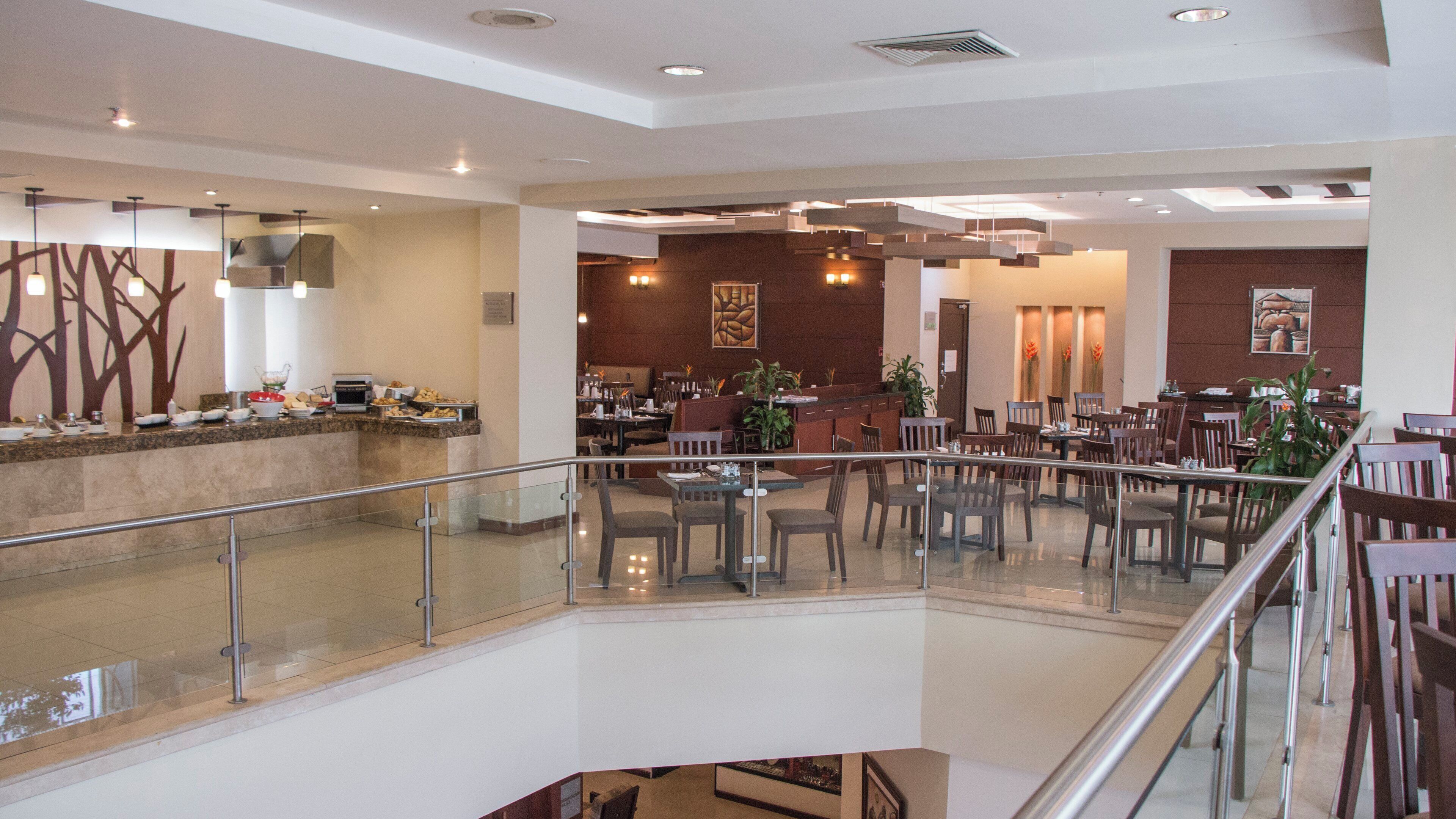 Un espace intérieur spacieux doté d’une rambarde en verre, de plusieurs tables et chaises, ainsi que d’un comptoir de buffet.