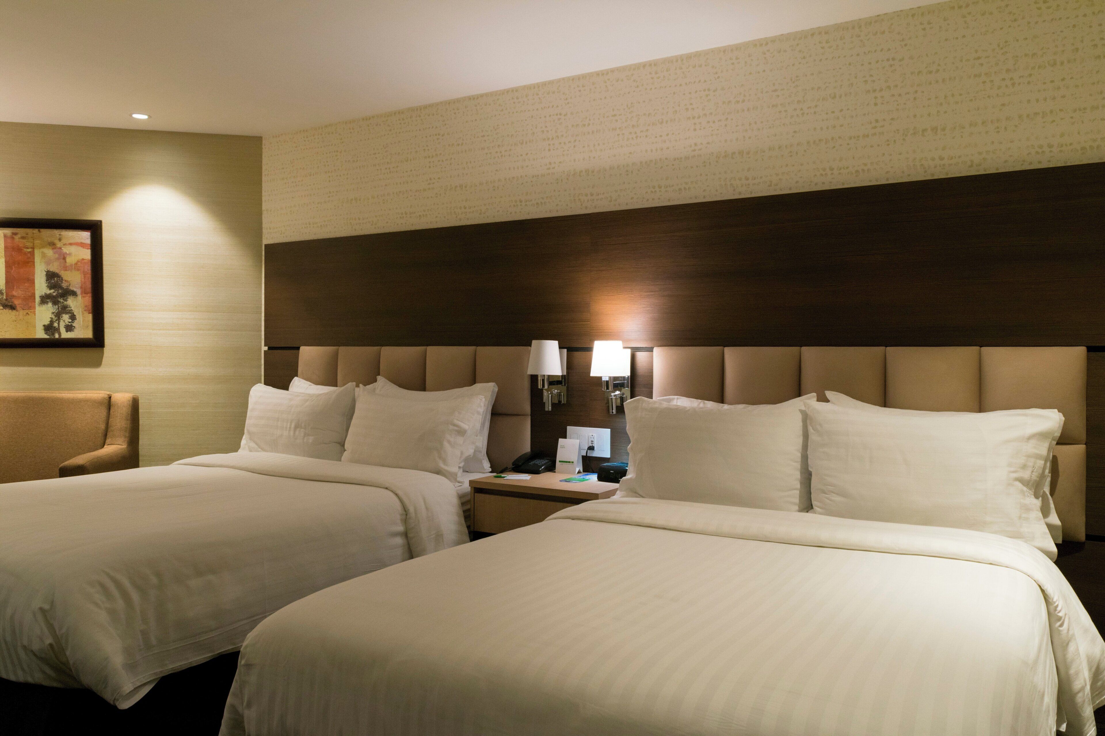 Habitación de hotel con dos camas, una mesita de noche, una lámpara y un cuadro en la pared.