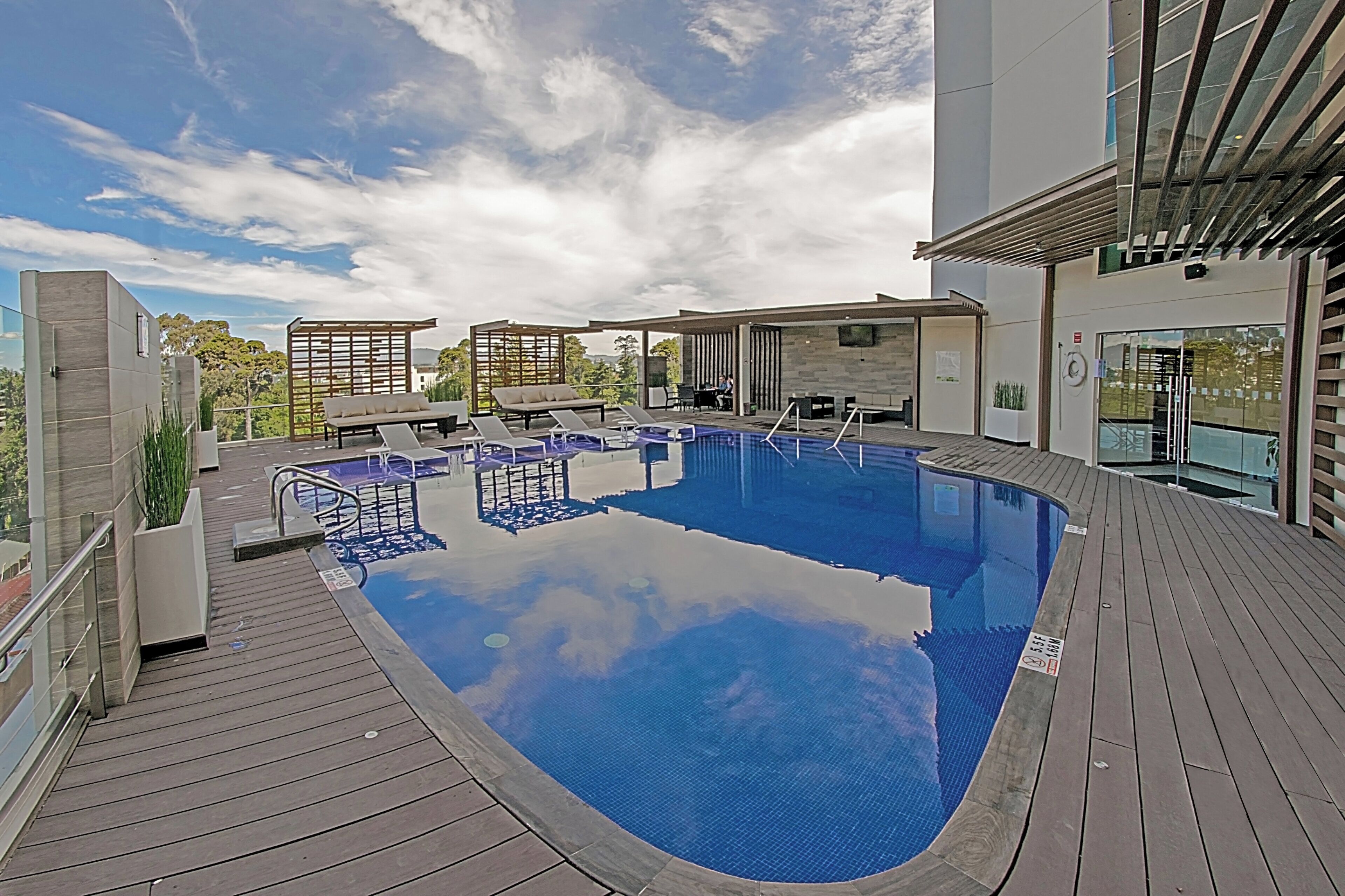 Una piscina en la azotea con sillones de descanso y terraza de madera.