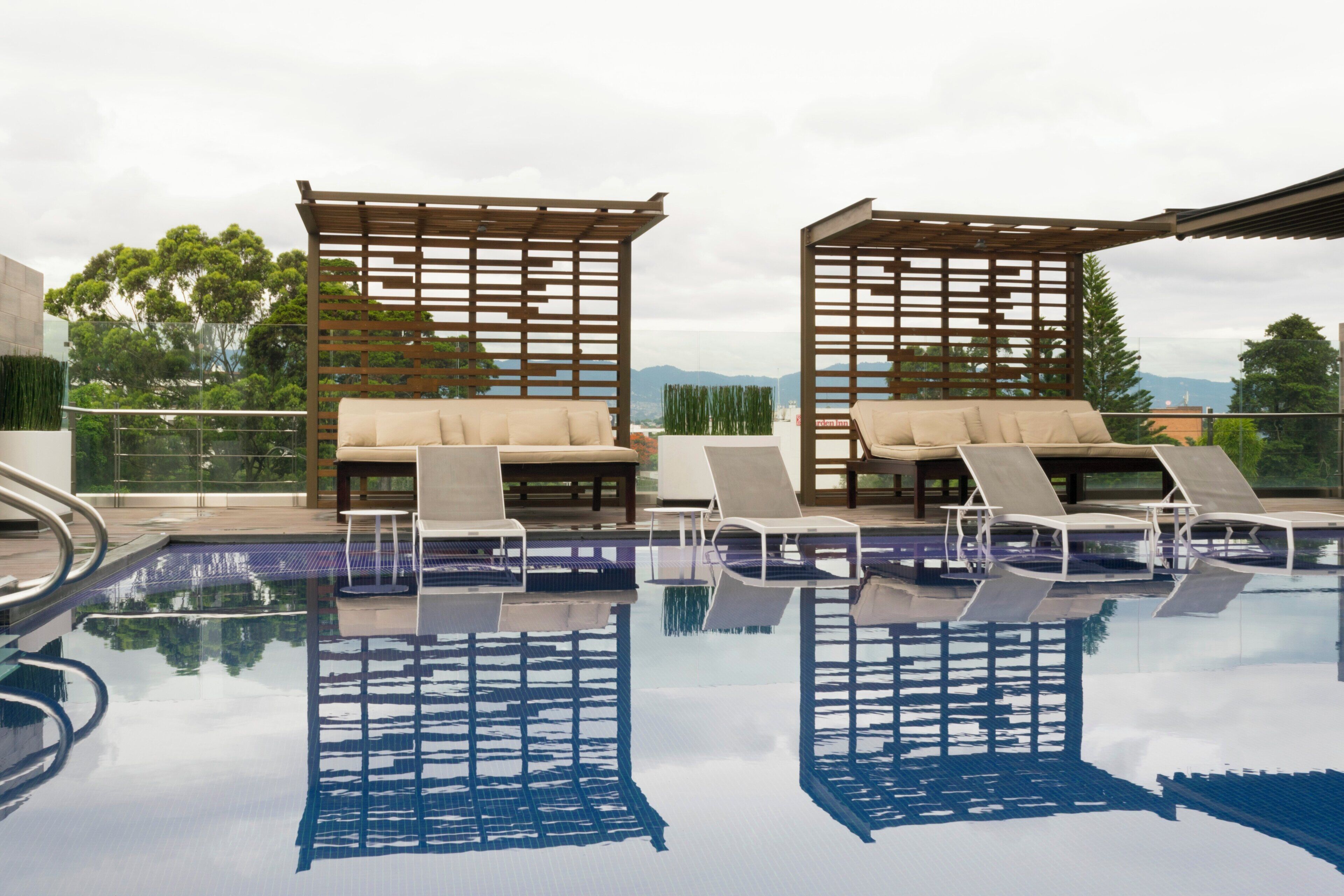 A rooftop pool area with lounge chairs and a wooden pergola.
