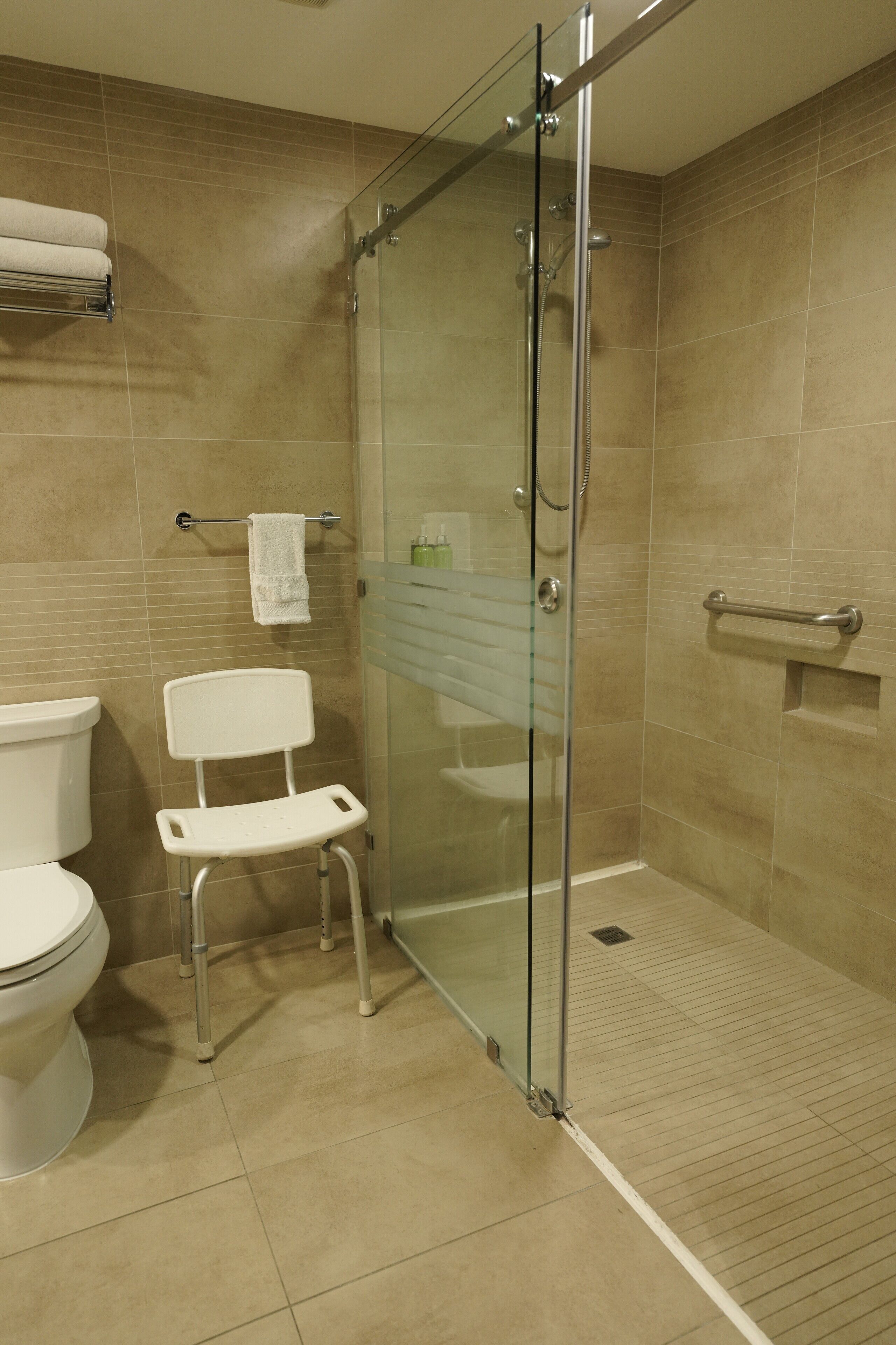 A modern bathroom with a glass-enclosed shower, a white toilet, and a white chair.