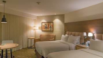 A hotel room with two beds, a desk, a chair, and a small table.