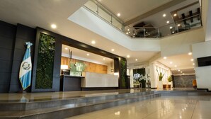 A modern hotel lobby with a reception desk, a flag, and a staircase leading to an upper level. - Holiday Inn Guatemala City by IHG (Guatemala City)
