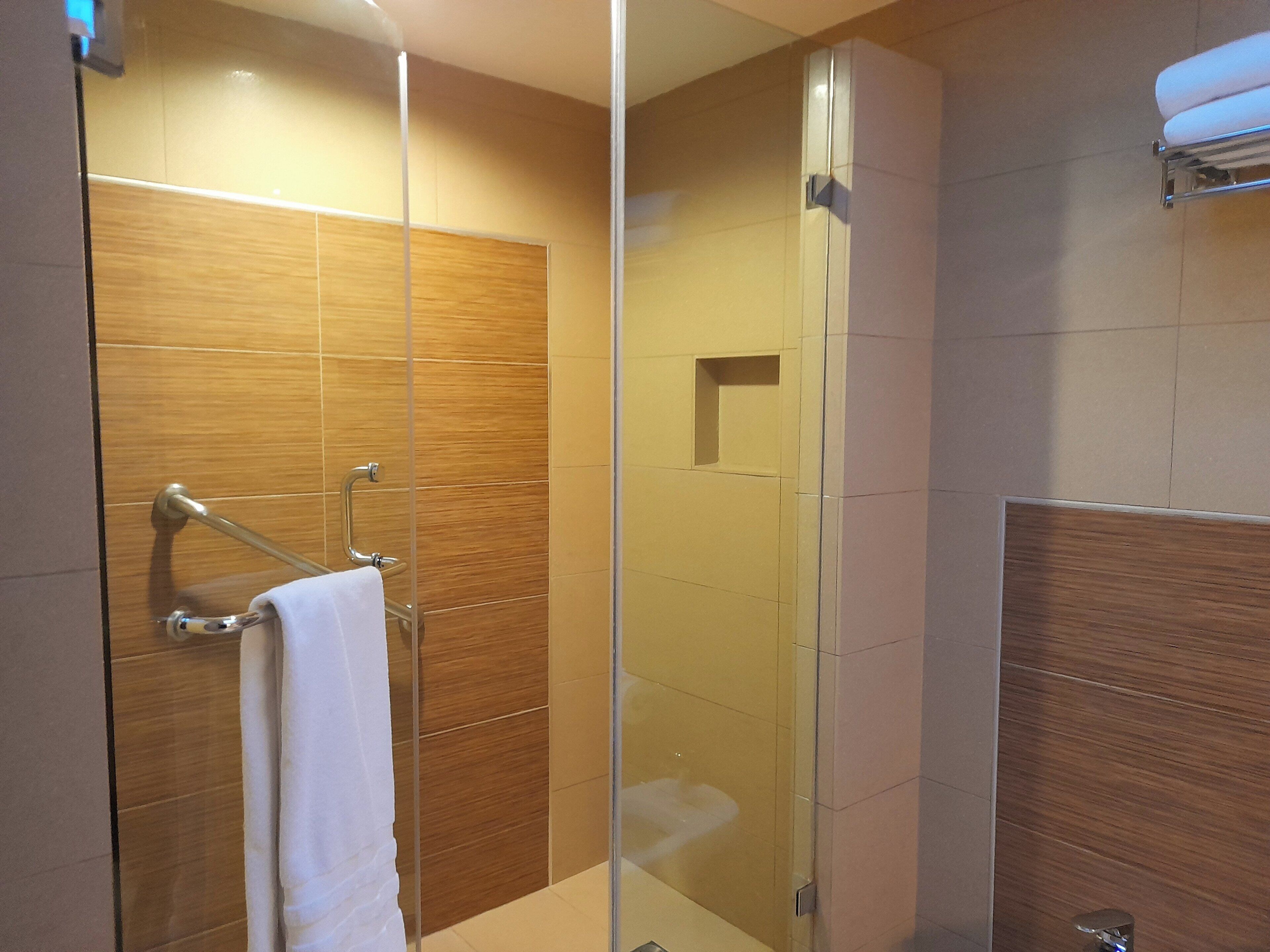 A modern bathroom with a glass shower enclosure, wooden paneling, and a towel rack.