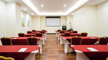 A conference room with rows of tables and chairs, a podium, and a projector screen.