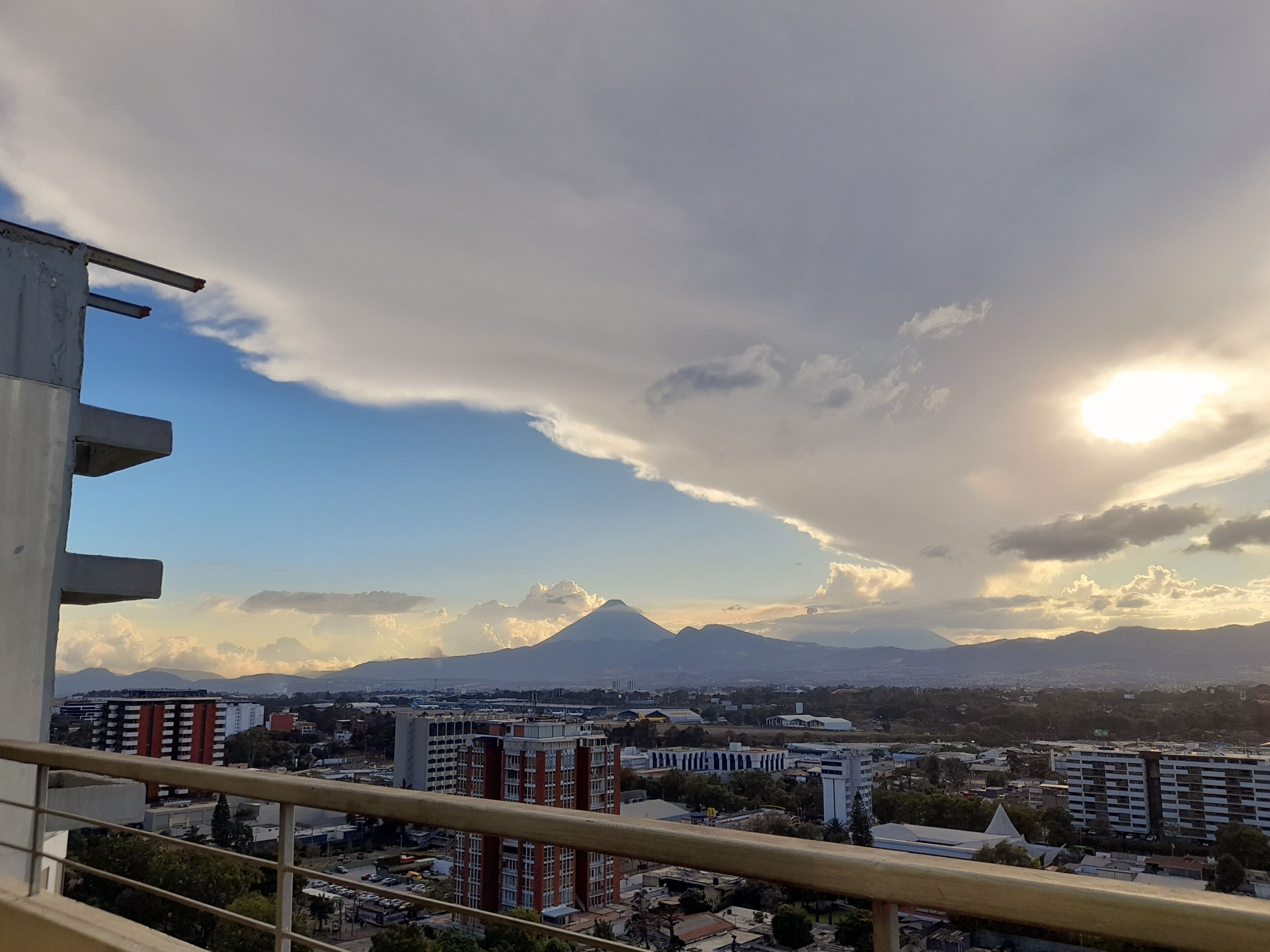 A cityscape with a prominent mountain in the background, buildings, and a clear sky with clouds.