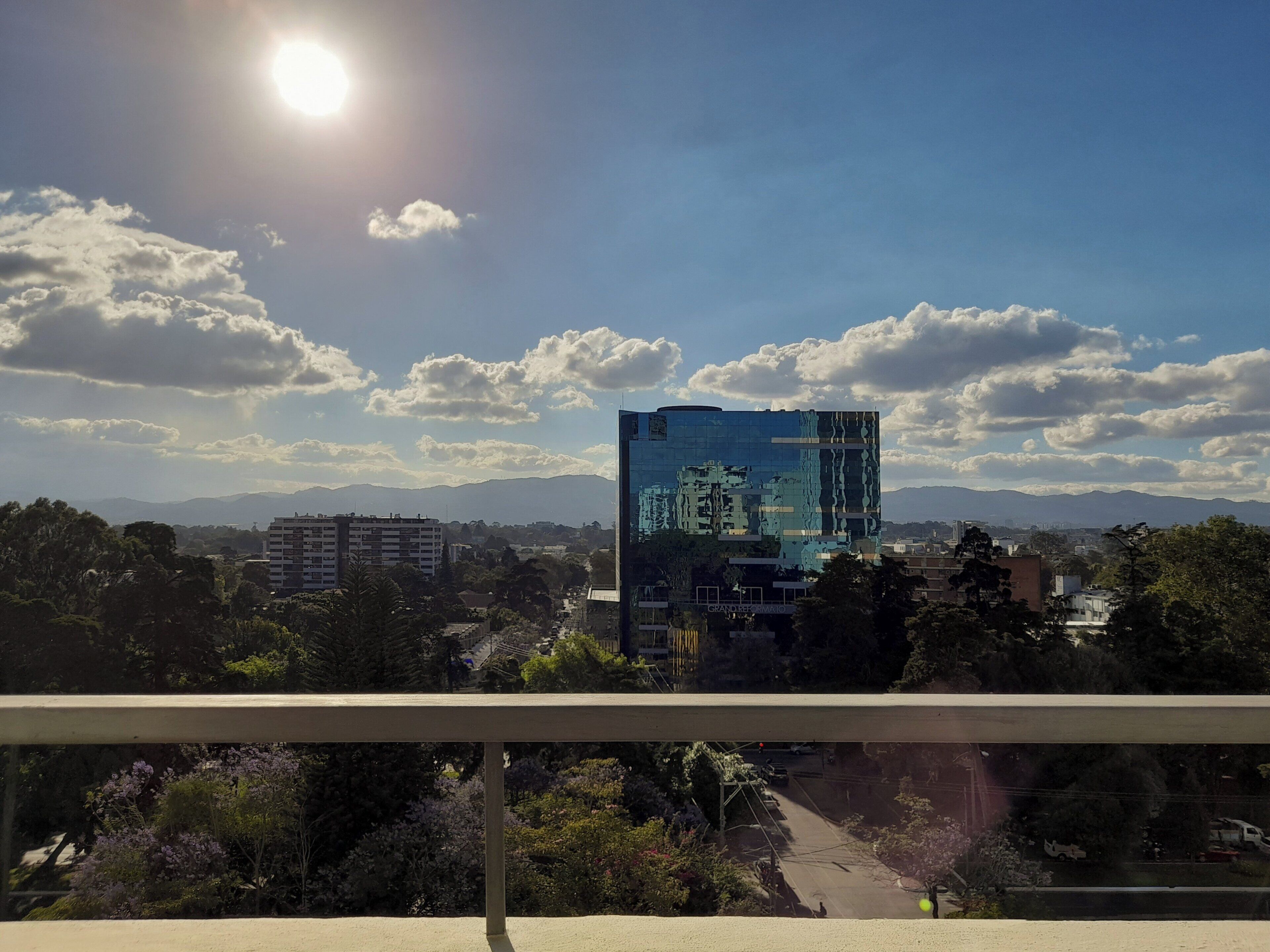 A cityscape with a prominent modern building, a clear sky, and distant mountains.