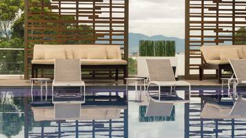 Zona de piscina con sillones de descanso y un sofá, rodeada por estructuras de celosía de madera.