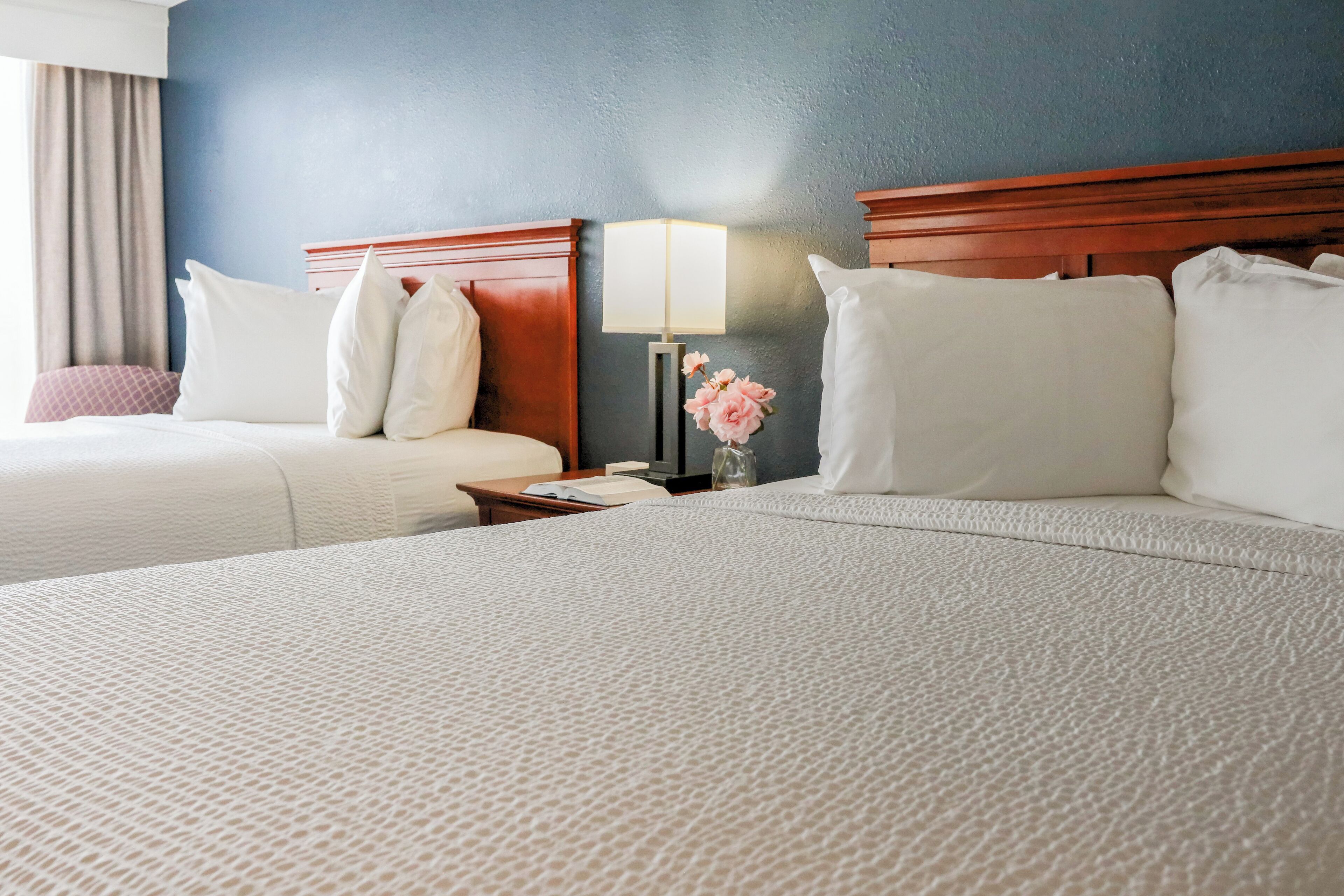 Une chambre d’hôtel avec deux lits, une table de chevet avec une lampe et un vase de fleurs.