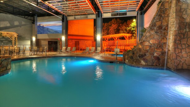 An indoor swimming pool with a stone wall and a mural of a landscape. - The Ramsey Hotel and Convention Center Pigeon Forge (Pigeon Forge)